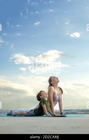 Mère et fils faisant de l'exercice sur le balcon à l'arrière-plan d'une ville au lever ou au coucher du soleil, concept d'un mode de vie sain