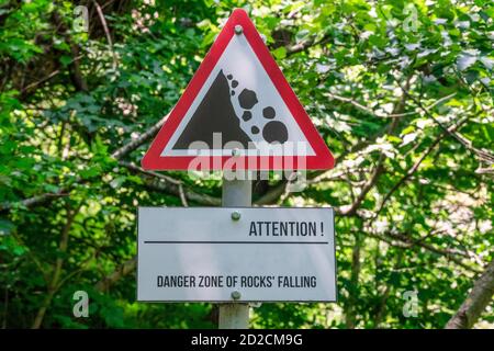 Gros plan d'un signe de chute possible de la roche des montagnes contre le fond des branches d'arbres, avertissement de danger Banque D'Images