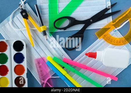 Fournitures scolaires et trois masques médicaux sur fond bleu. Banque D'Images