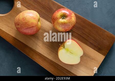 Deux pommes entières et une moitié se trouvent sur la planche à découper. Banque D'Images
