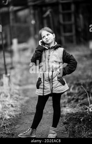 Petite fille mignonne parlant sur mobile, en plein air dans le village. Photographie en noir et blanc. Banque D'Images