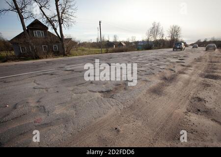 Route de mauvaise qualité avec des nids-de-poule, des voitures en arrière-plan, la campagne. Trou dans l'asphalte. Fosse, non sécuritaire, route du trou. Transport, destruction des routes, risque o Banque D'Images