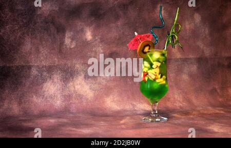 Un verre de jus à base de kiwi avec glace, morceaux de fruits, parapluie et pailles. Gros plan. Banque D'Images