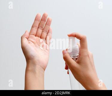 Mains d'une femme utilisant un spray désinfectant sur fond gris Banque D'Images