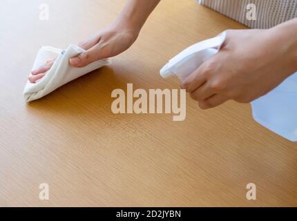 Les mains d'une femme se vaporisent pour nettoyer une table. Banque D'Images