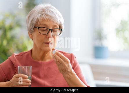 Femme âgée tenant une pilule et un verre d'eau douce, prenant des médicaments contre les maux de tête, les douleurs à l'estomac ou prenant des vitamines, des médicaments de sédation. Banque D'Images