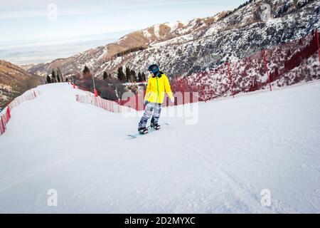 Belle jeune femme en blouson jaune apprend à faire du snowboard. Banque D'Images