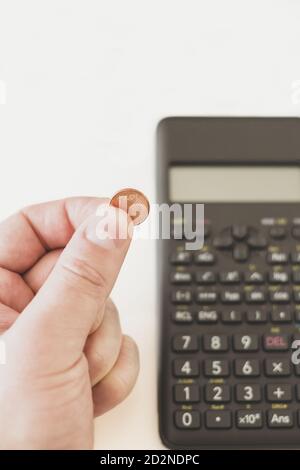 Photo verticale d'une main tenant une pièce d'un cent d'euro à côté d'une calculatrice avec un fond blanc Banque D'Images