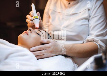 Femme brune couchée ayant des procédures de traitement du visage au salon de spa utilisation d'appareils modernes Banque D'Images