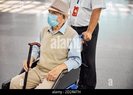 Employé de l'aéroport roulant en fauteuil roulant avec une personne handicapée Banque D'Images