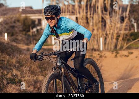 Sportswoman en casque noir et vêtements de sport bleus avec lunettes de vélo de montagne sur la piste d'entraînement Banque D'Images