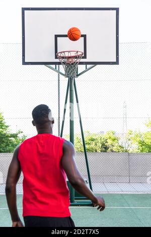 Vue arrière d'un homme afro-américain méconnu jouant au basket-ball terrain de sport moderne pendant l'entraînement Banque D'Images