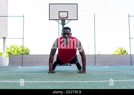 Joueur de basket-ball masculin noir déterminé qui fait des retouches pendant intense entraînement sur terrain de sport et regarder la caméra Banque D'Images