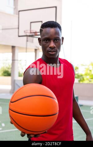 Joueur de basket-ball déterminé debout avec un ballon sur le terrain de jeu l'été et regarder l'appareil photo Banque D'Images