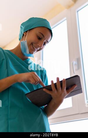 Jeune infirmière en gommages bleus et informations de lecture de masque médical sur une tablette dans un couloir de l'hôpital moderne Banque D'Images