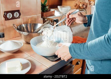 Rognez un mâle anonyme en ajoutant de la farine dans un bol placé sur des balances tout en préparant des ingrédients pour biscuits pâte dans la cuisine maison Banque D'Images