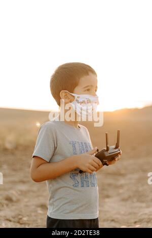 Petit garçon asiatique dans un masque de protection utilisant la télécommande pendant jouer avec un drone volant sur le terrain Banque D'Images