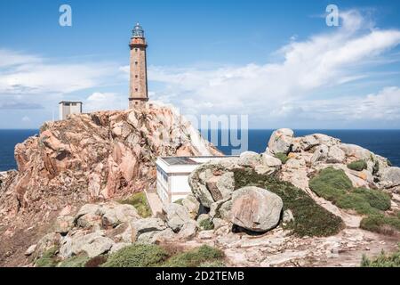 Paysage pittoresque avec ancienne tour de phare et maisons situées sur Falaise rocheuse rugueuse près de la mer sur la péninsule du Cap Vilan Côte espagnole contre ciel bleu ciel nuageux en été Banque D'Images