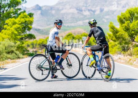 Vue arrière du corps de l'homme et de la femme sportive heureux en casque d'activité et casques debout avec des vélos sur la chaussée d'asphalte et se reposant pendant le trajet à travers Banque D'Images