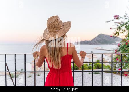 Vue arrière d'une touriste féminine méconnue debout avec chapeau de paille dans la main levée sur la terrasse et profiter des vacances d'été pendant admirez le paysage urbain incroyable Banque D'Images