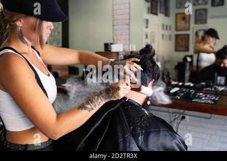 Professionnel femelle hipster application de talc poudre sur le cou de l'homme client après la procédure de rasage dans un salon de coiffure moderne Banque D'Images