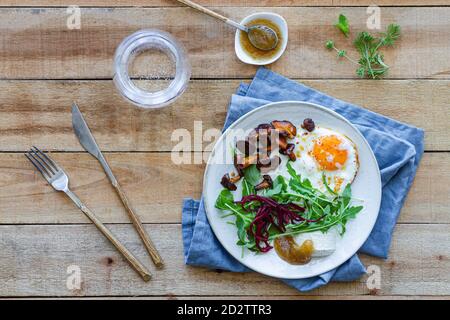 Vue de dessus de l'assiette avec un œuf plat délicieux servi avec champignons et salade fraîche sur table en bois avec sauce et verre d'eau Banque D'Images