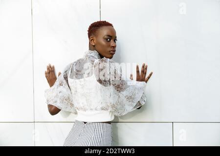 Une petite image de derrière de jeunes Afro-américains confiants et minces femme dans un élégant chemisier et pantalon debout contre le mur de bâtiment moderne et vue sur la caméra Banque D'Images