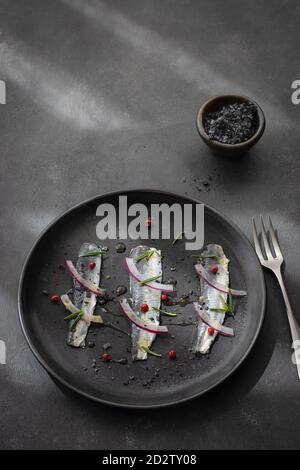 Vue de dessus de l'appétissant filet de poisson de sardines marinées avec oignon et herbes servies sur plaque noire avec fourchette Banque D'Images