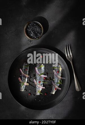 Vue de dessus de l'appétissant filet de poisson de sardines marinées avec oignon et herbes servies sur plaque noire avec fourchette Banque D'Images