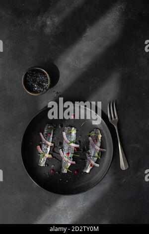 Vue de dessus de l'appétissant filet de poisson de sardines marinées avec oignon et herbes servies sur plaque noire avec fourchette Banque D'Images