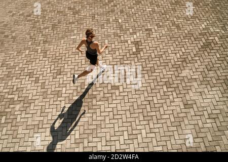 Du haut du corps de la femme active et mince dans les vêtements de sport course rapide sur la place pavée par beau temps Banque D'Images