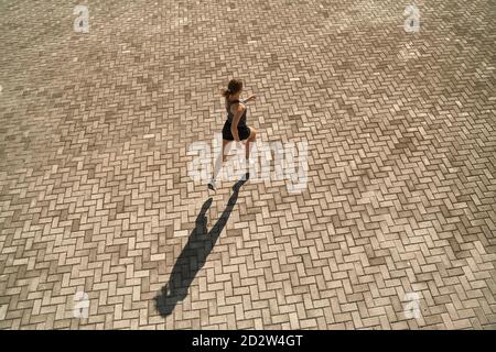 Du haut du corps de la femme active et mince dans les vêtements de sport course rapide sur la place pavée par beau temps Banque D'Images