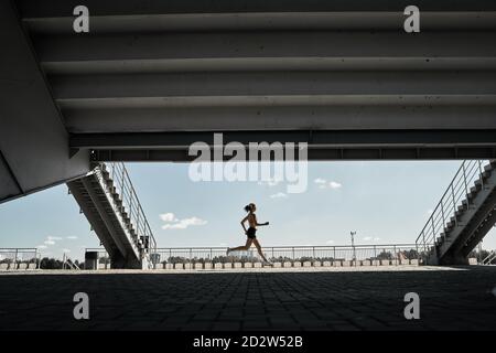 Vue latérale d'une athlète féminine déterminée qui court rapidement en plein air faites de l'exercice près des escaliers du stade Banque D'Images