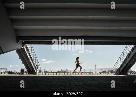 Vue latérale d'une athlète féminine déterminée qui court rapidement en plein air faites de l'exercice près des escaliers du stade Banque D'Images