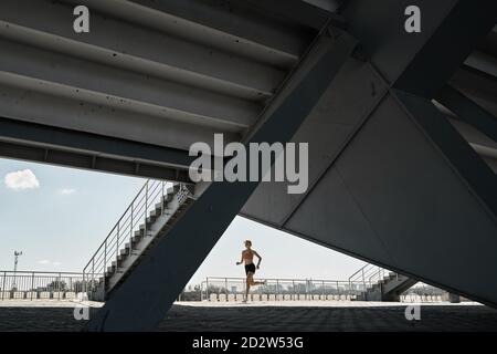 Vue latérale d'une athlète féminine déterminée qui court rapidement en plein air faites de l'exercice près des escaliers du stade Banque D'Images