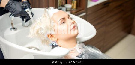 Coiffeur Préparez-vous à laver la teinture blanche des cheveux de la jeune femme caucasienne dans le lavabo au salon de beauté Banque D'Images