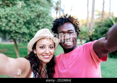 Couple de voyage multiracial enjoué et emportant le selfie sur un smartphone pendant vos vacances d'été, vous vous tenez dans un parc tropical verdoyant Banque D'Images