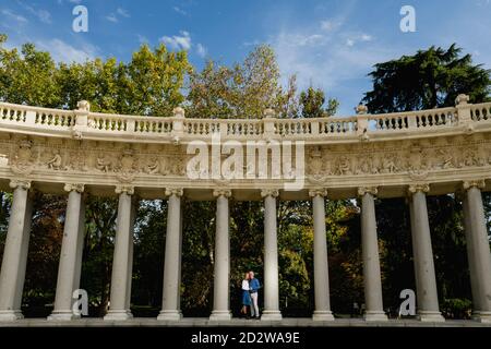 Vue à distance d'un couple se tenant debout sur la pierre colonnes de passage voûté dans le parc urbain pendant la promenade estivale Banque D'Images