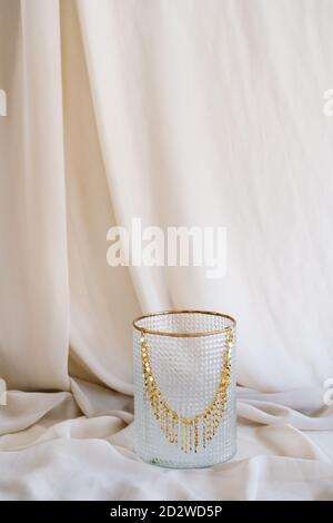 Collier brillant élégant en or placé sur un support en verre sur un morceau de tissu en studio Banque D'Images