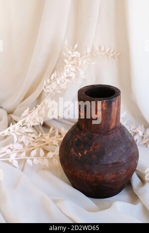 Vieux vase en argile fait main placé sur un morceau de tissu avec plante séchée en studio Banque D'Images