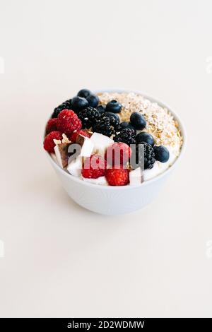 Grand angle de bol nutritif avec muesli et diverses baies dans un bol placé sur une table blanche pour le petit déjeuner le matin Banque D'Images