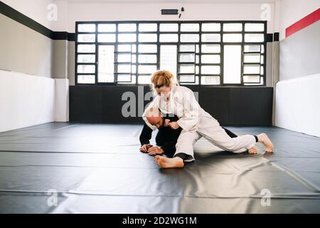 Trois partenaires dans une formation en arts martiaux comme le judo ou karaté avec des kimonos pratiquant les techniques sur le tapis de gym tous les masques de port en raison de la c Banque D'Images