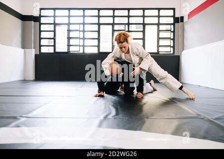 Trois partenaires dans une formation en arts martiaux comme le judo ou karaté avec des kimonos pratiquant les techniques sur le tapis de gym tous les masques de port en raison de la c Banque D'Images