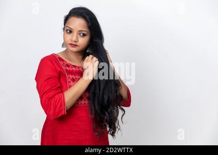 Portrait d'une femme indienne avec les doigts dans ses cheveux longs, cheveux foncés, toile de fond blanche, prise en studio en intérieur, zone de copie. Banque D'Images