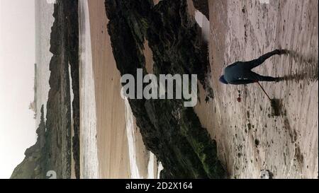 Une figure solitaire dégage le pétrole de la plage à angle Bay, Pembrokeshire, tandis que le pétrolier frappé Sea Express liste en arrière-plan. Banque D'Images