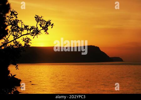 Coucher de soleil orange sur la mer. Le soleil se couche magnifiquement sur la crête de la montagne. Vue sur la mer avec une silhouette de colline à Bay. Banque D'Images