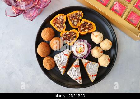 Assortiment de sucreries indiennes ou Mithai, Rava laddoo, Besan laddu, sucreries aux fruits secs dans une assiette noire avec chocolats Happy Diwali pour le festival de Diwali. Banque D'Images