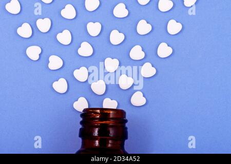 Pilules en forme de coeur de verre de bouteille sur un fond bleu. Des médicaments qui aident les gens. Banque D'Images