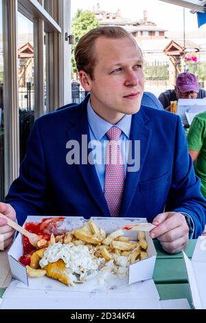 A Young Man Eating Fish and Chips, Londres, Royaume-Uni. Banque D'Images