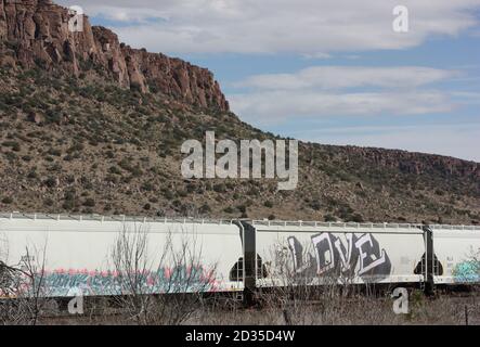 Voitures de chemin de fer Graffitied du train d'amour alignées l'horizon contre le rocher rouge butte sous ciel bleu clair Banque D'Images